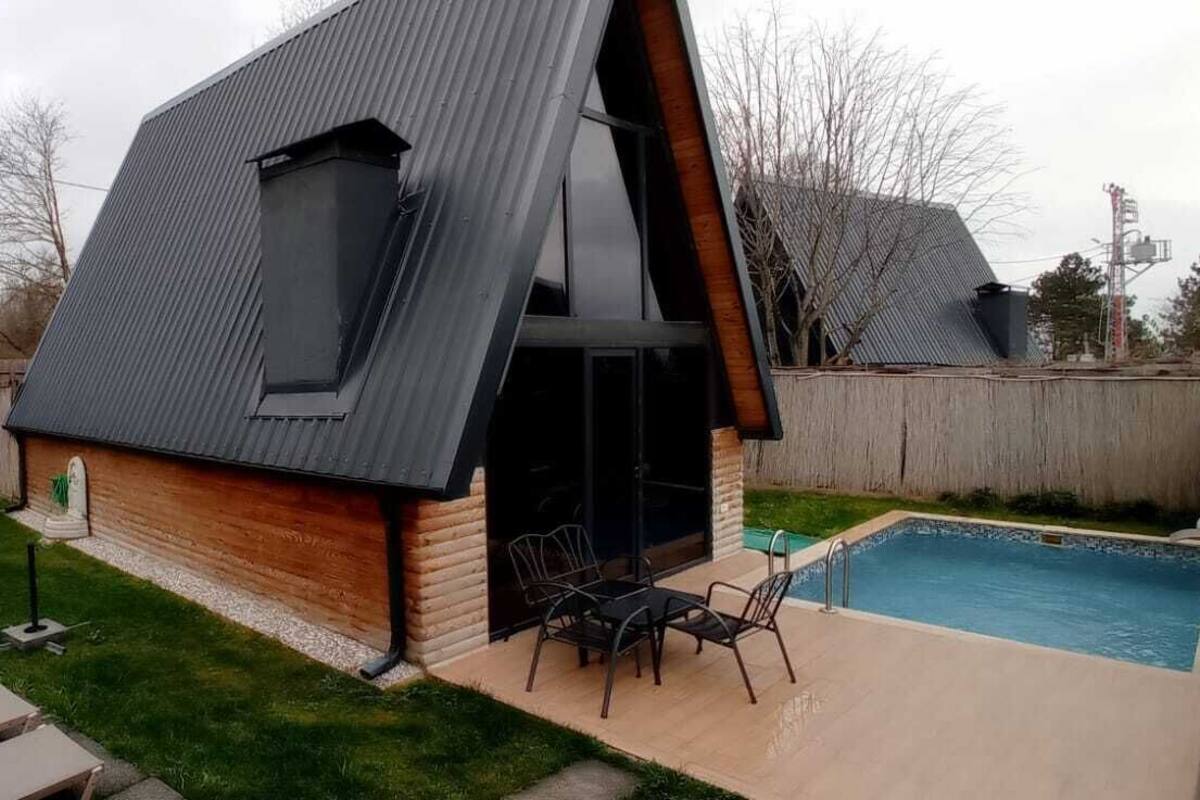 A modern house with a sloped roof, a swimming pool, and a patio with outdoor furniture.