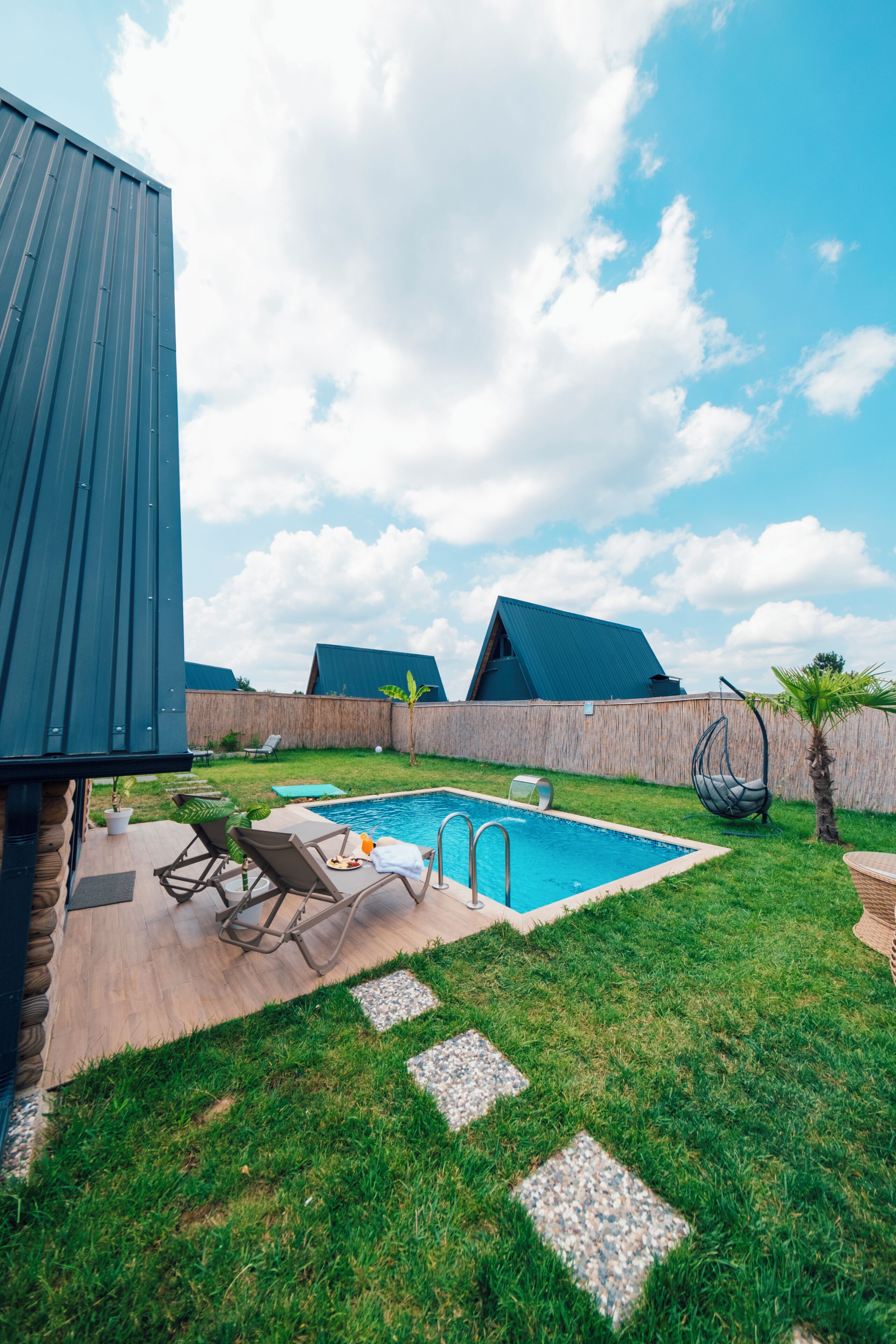 A backyard with a swimming pool, lounge chairs, and a hanging chair.
