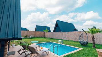 A backyard with a swimming pool, lounge chairs, and a hanging chair.