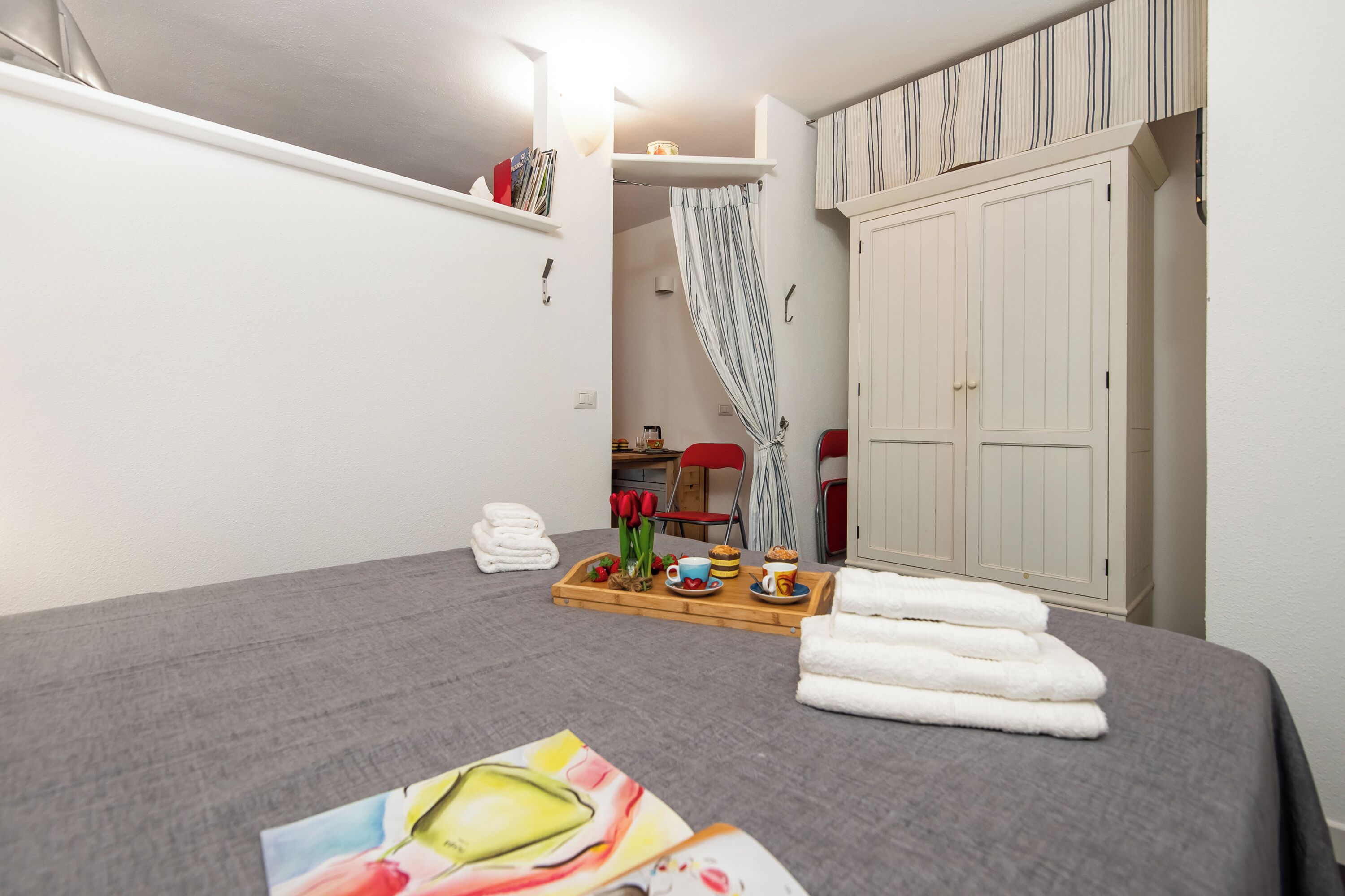 A hotel room with a bed, a tray with towels and a breakfast tray, a wardrobe, and a shower area.