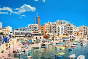 A coastal cityscape with a marina, buildings, and a prominent tower.