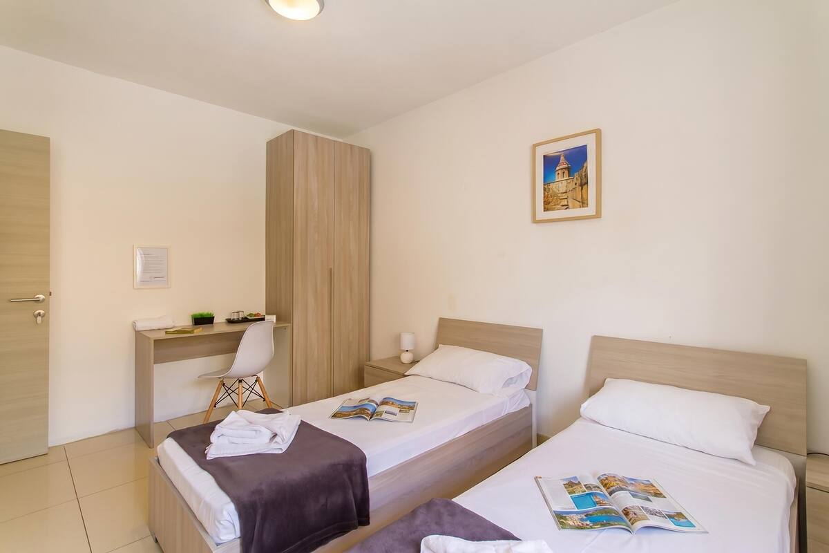 Habitación de hotel con dos camas, un escritorio, una silla y una mesita de noche.