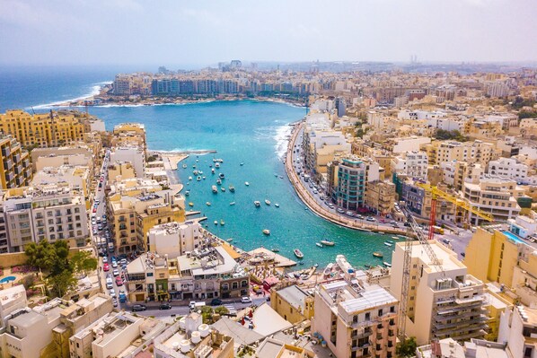 A coastal cityscape with a marina, buildings, and a clear view of the sea.