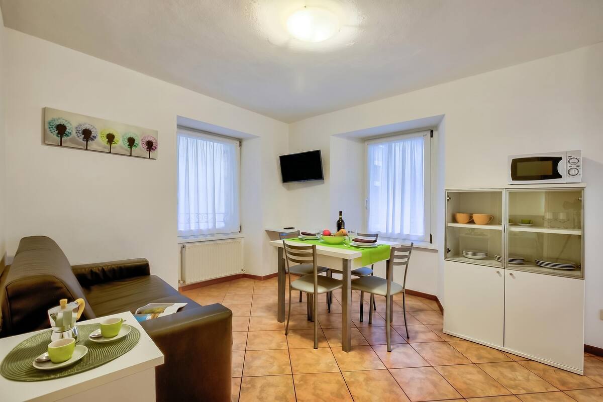 Un salon comprenant un canapé, une table à manger avec des chaises, un téléviseur et un coin cuisine équipé d’un four à micro-ondes et de placards.
