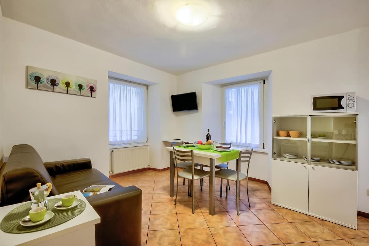 A living room with a sofa, a dining table with chairs, a television, and a kitchen area with a microwave and cabinets.