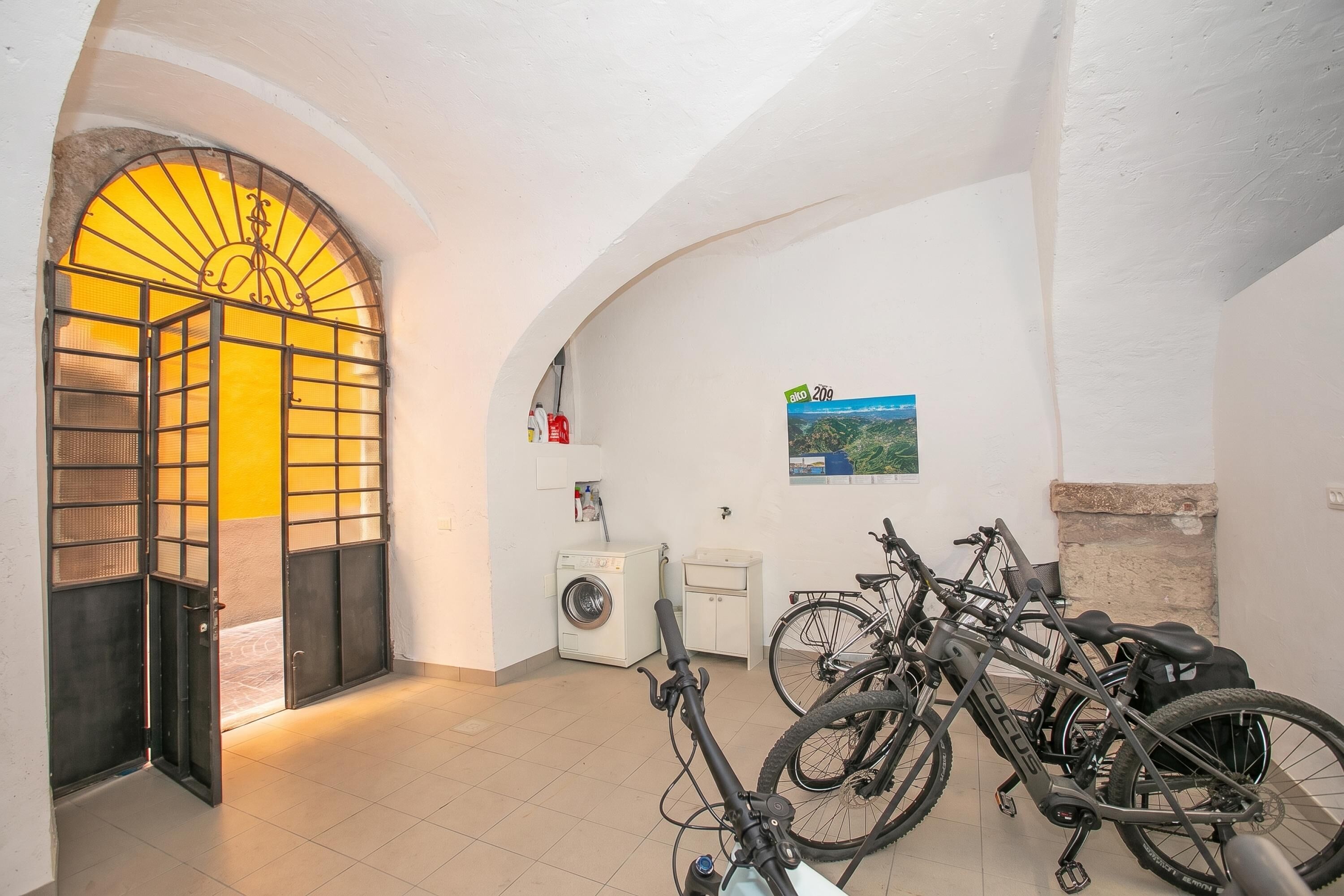 A room with a washing machine, a bicycle, and a door with a sunlit archway.
