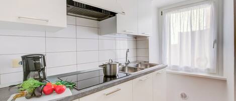A modern kitchen with white cabinets, a black countertop, a coffee maker, a pot, and fresh vegetables.