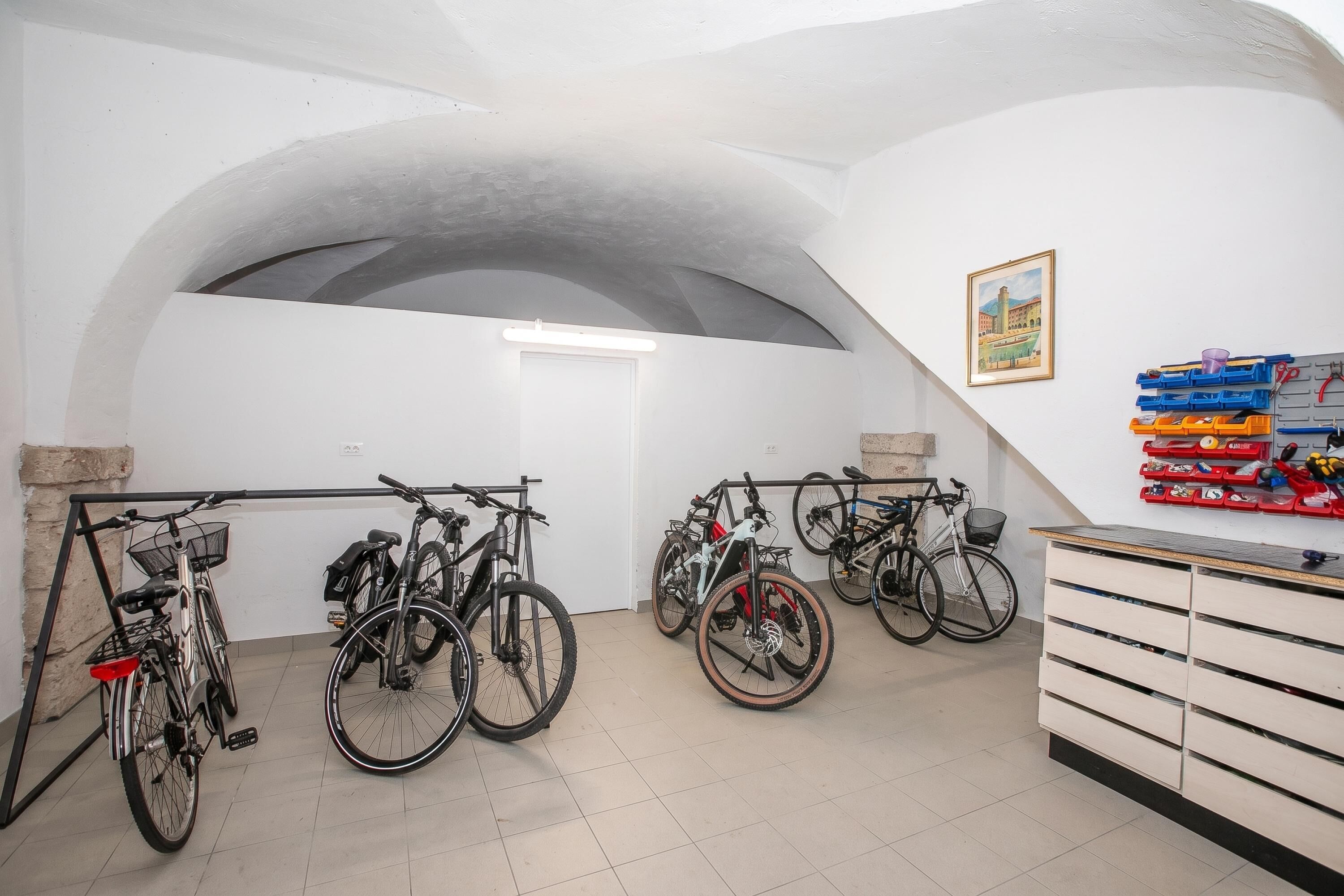 A bicycle storage area with multiple bikes, a white wall, and a door.