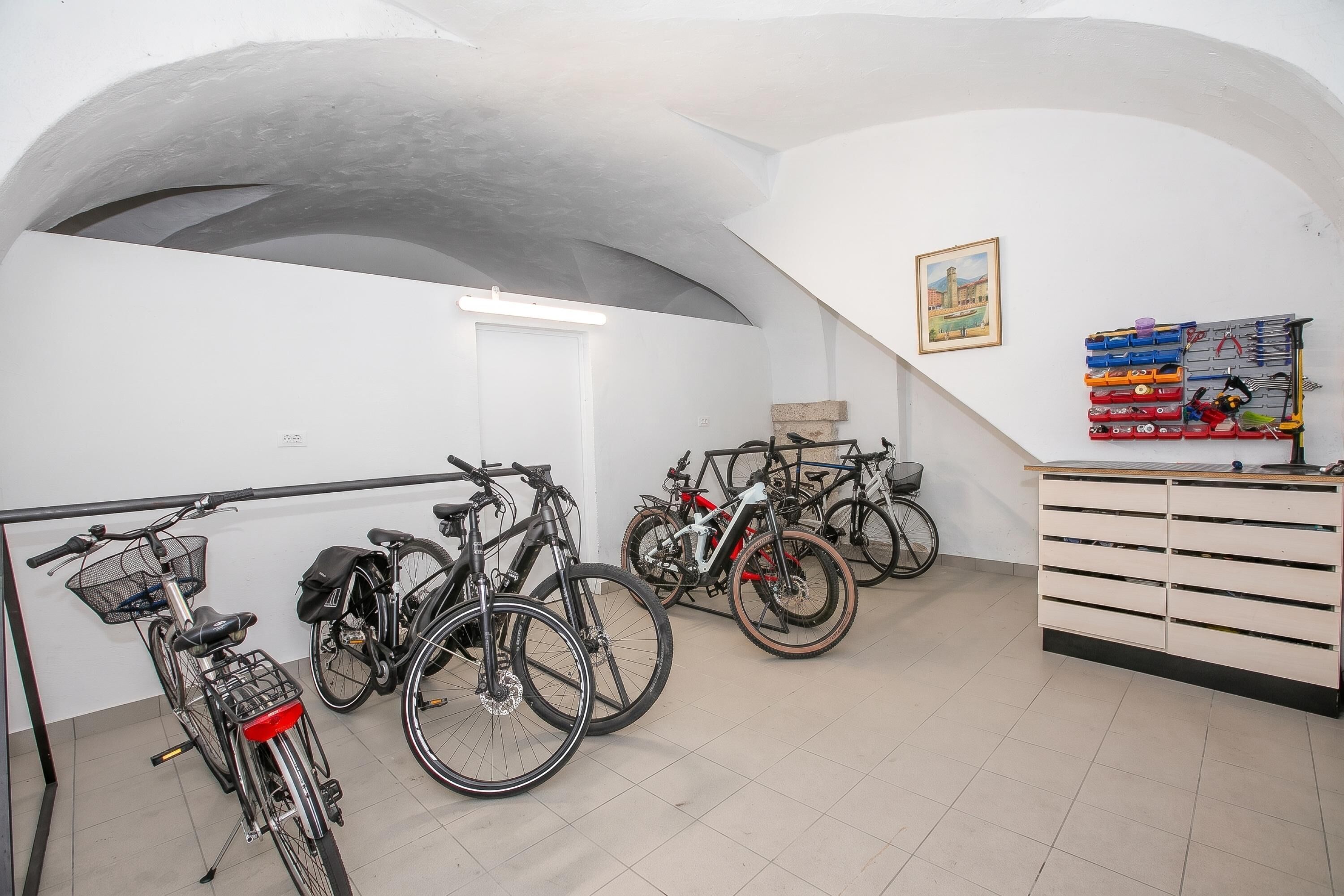 Ein Zimmer mit Fahrrädern, einer weißen Wand, einer Decke mit einem großen Bogen und einem wandmontierten Kastenregal.