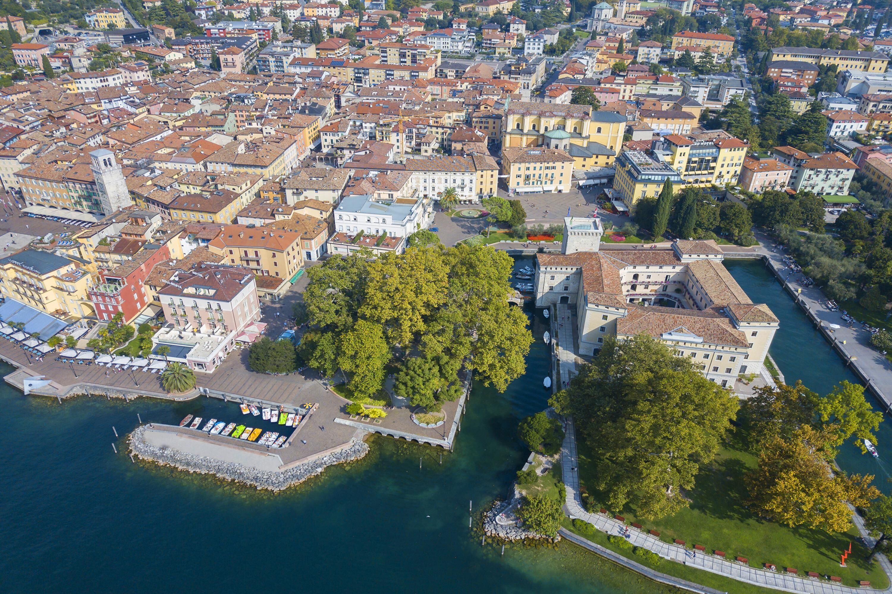 Une vue aérienne d’une zone urbaine densément peuplée, avec un front de mer bien visible, un grand arbre et un bâtiment historique doté d’une tour.