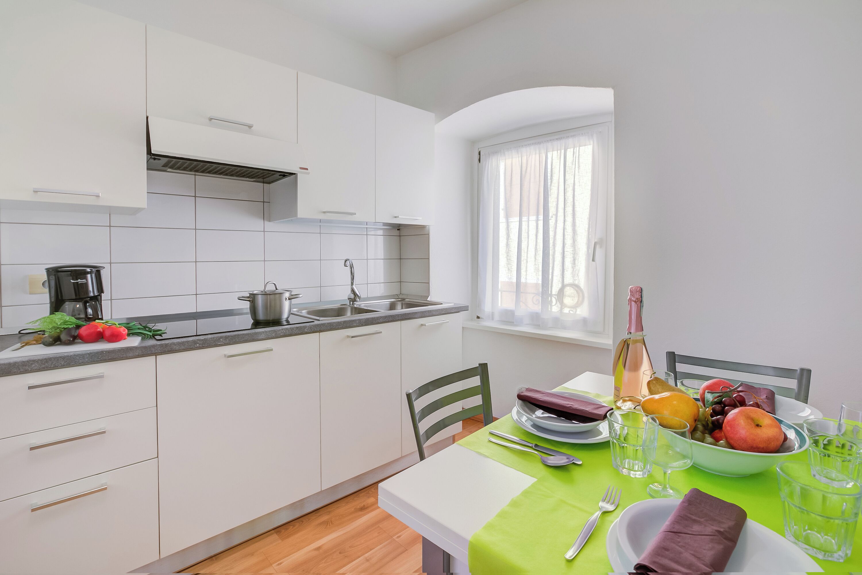 Una cucina moderna con mobili bianchi, un lavandino e una finestra con tende leggere.