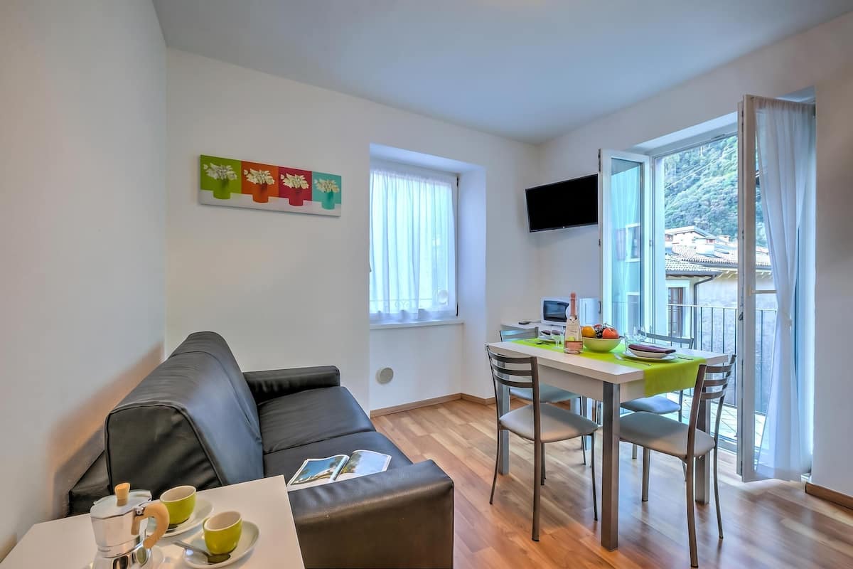 Un salon moderne avec un canapé, une table à manger et des chaises, une machine à café et un téléviseur fixé au mur.