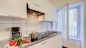 Une cuisine moderne avec des meubles blancs, un plan de travail noir, une machine à café, une casserole et des légumes frais.
