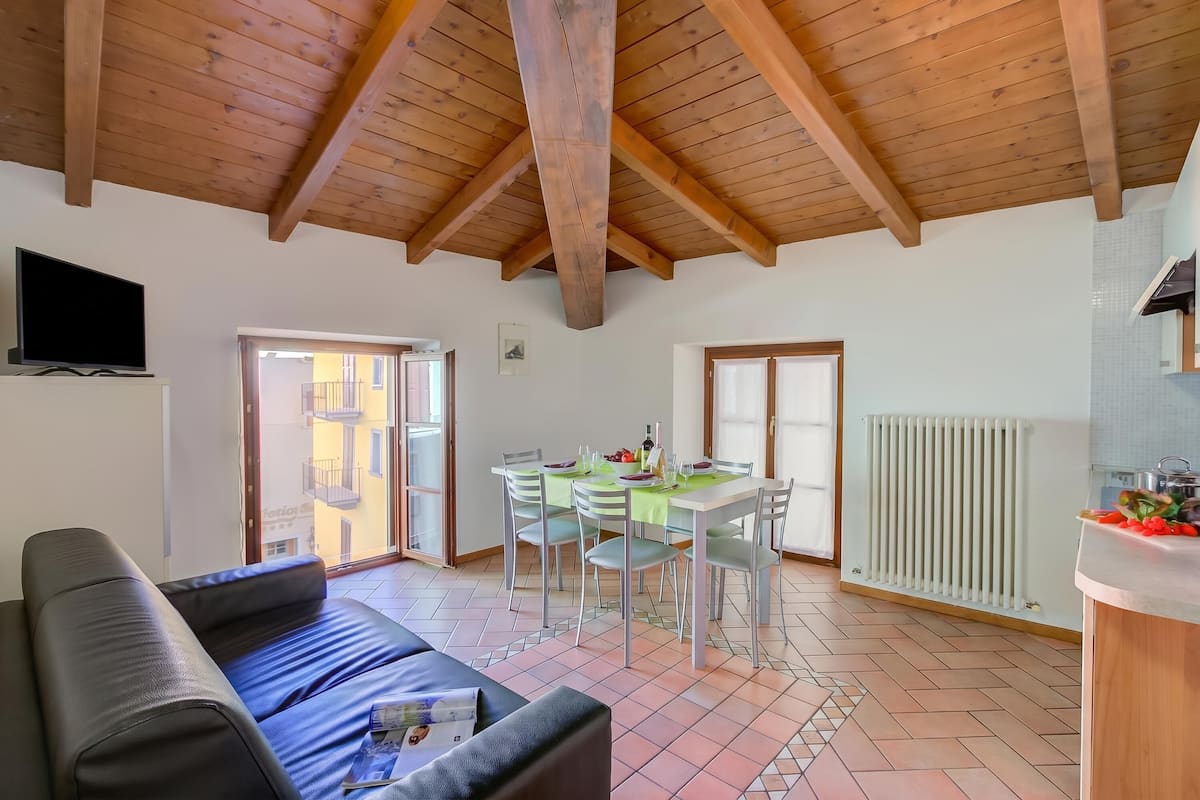 Un salon avec un canapé, une table à manger avec des chaises, un coin cuisine avec un comptoir et un téléviseur fixé au mur.