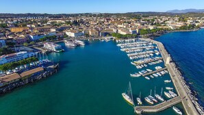 Une vue aérienne d’une marina où sont amarrés de nombreux bateaux, avec un grand navire de croisière et un paysage urbain en arrière-plan.