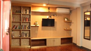 Een woonkamer met een houten boekenkast, een flatscreen televisie en een ingebouwde airconditioning.