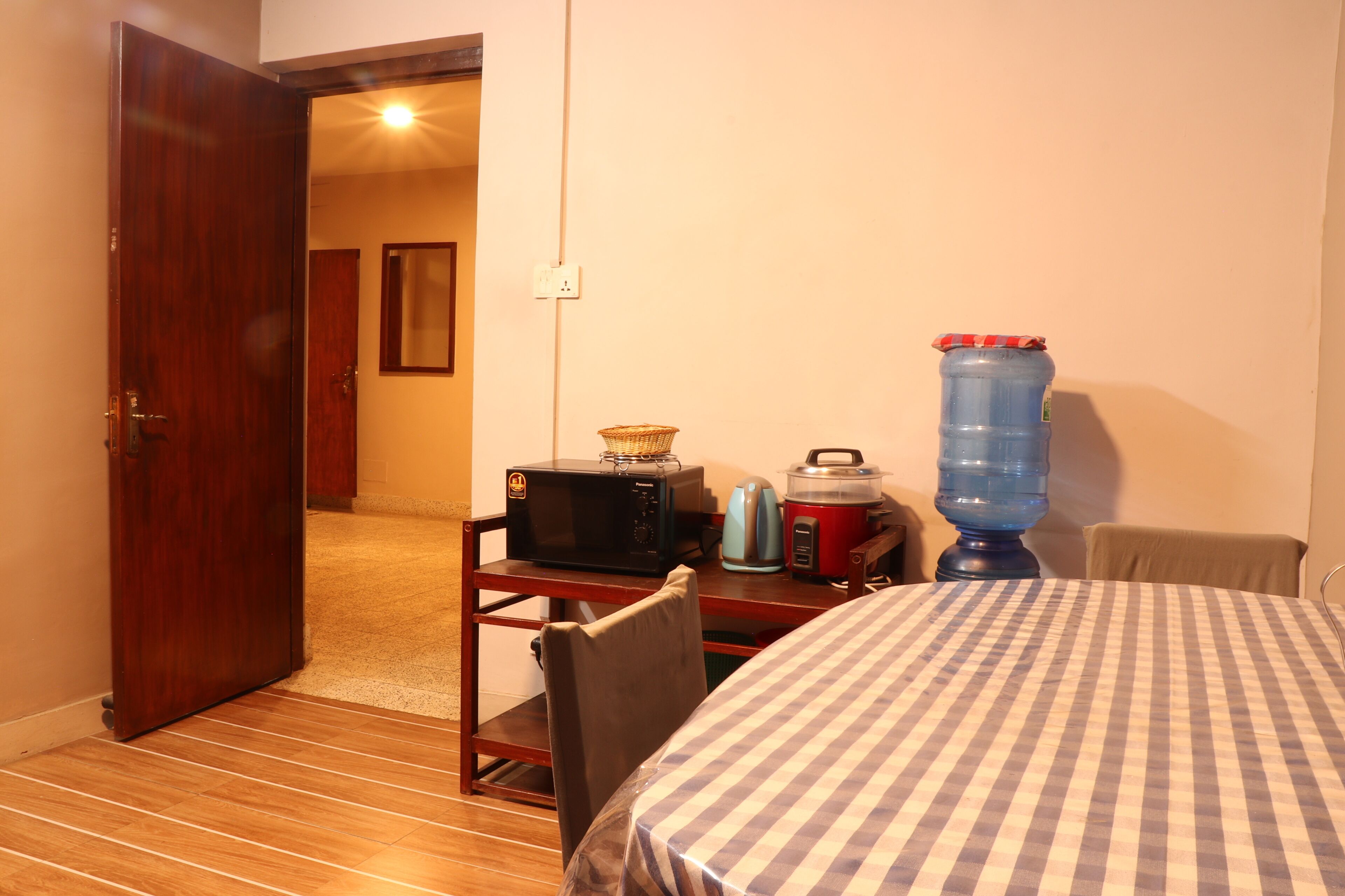 A room with a wooden door, a microwave on a small table, a water dispenser, and a checkered tablecloth.