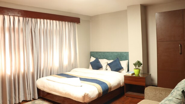 Een hotelkamer met een bed, nachtkastje, een bloempot en een kledingkast.