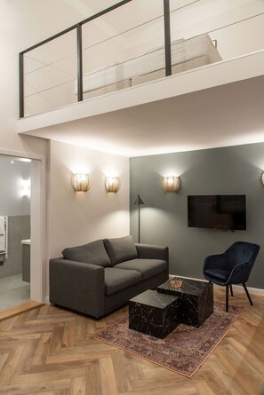 A modern living room with a grey sofa, a black coffee table, and a blue armchair. There is a TV mounted on the wall and a staircase leading to an upper level. - Budaguide A10-1 Central ideal for 4-6 people (Budapest)