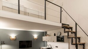 Un loft moderno con un entrepiso para el dormitorio, una cocina con armarios blancos, una zona de comedor y una escalera.