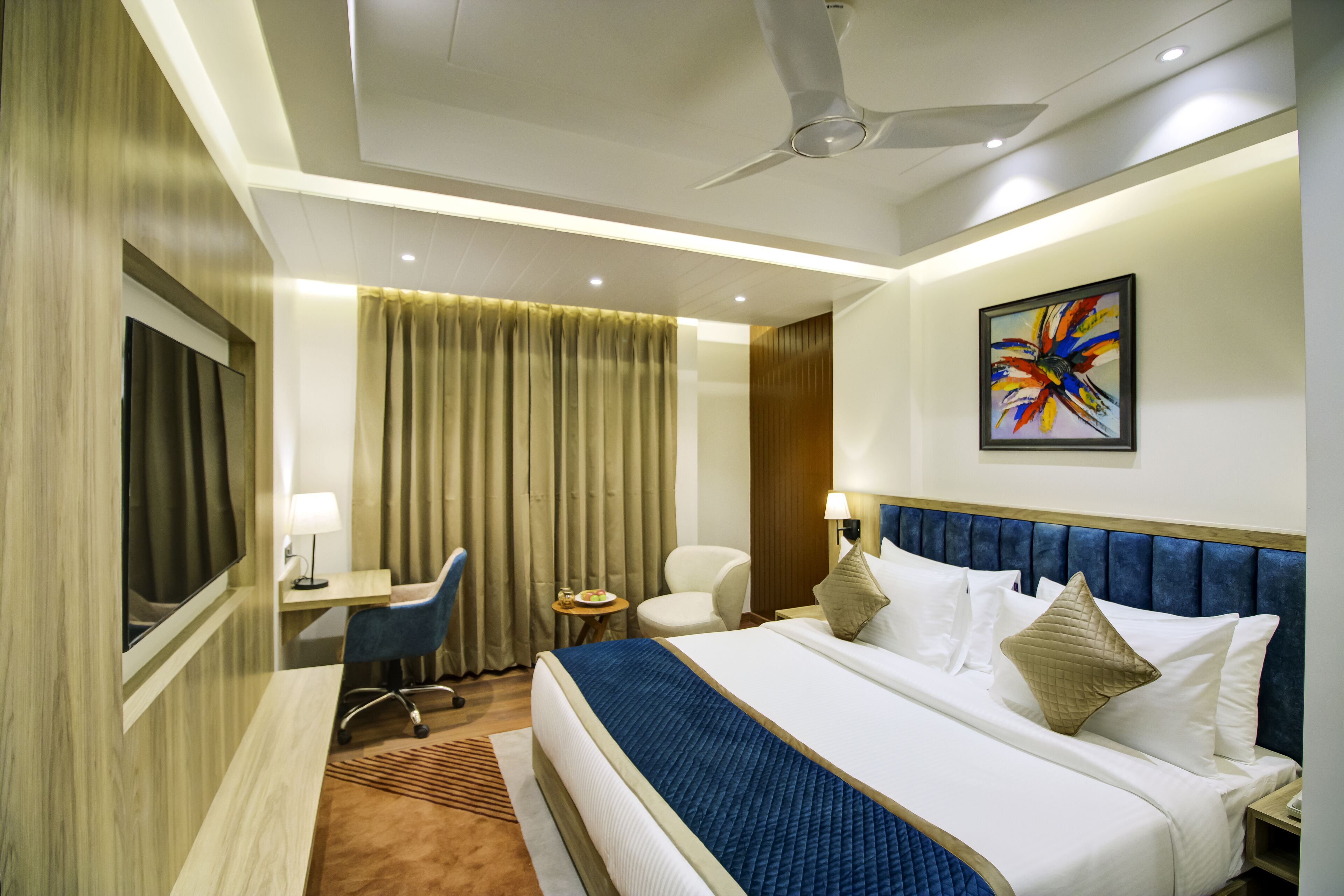 A hotel room with a bed, a desk, a chair, a TV, and a ceiling fan.
