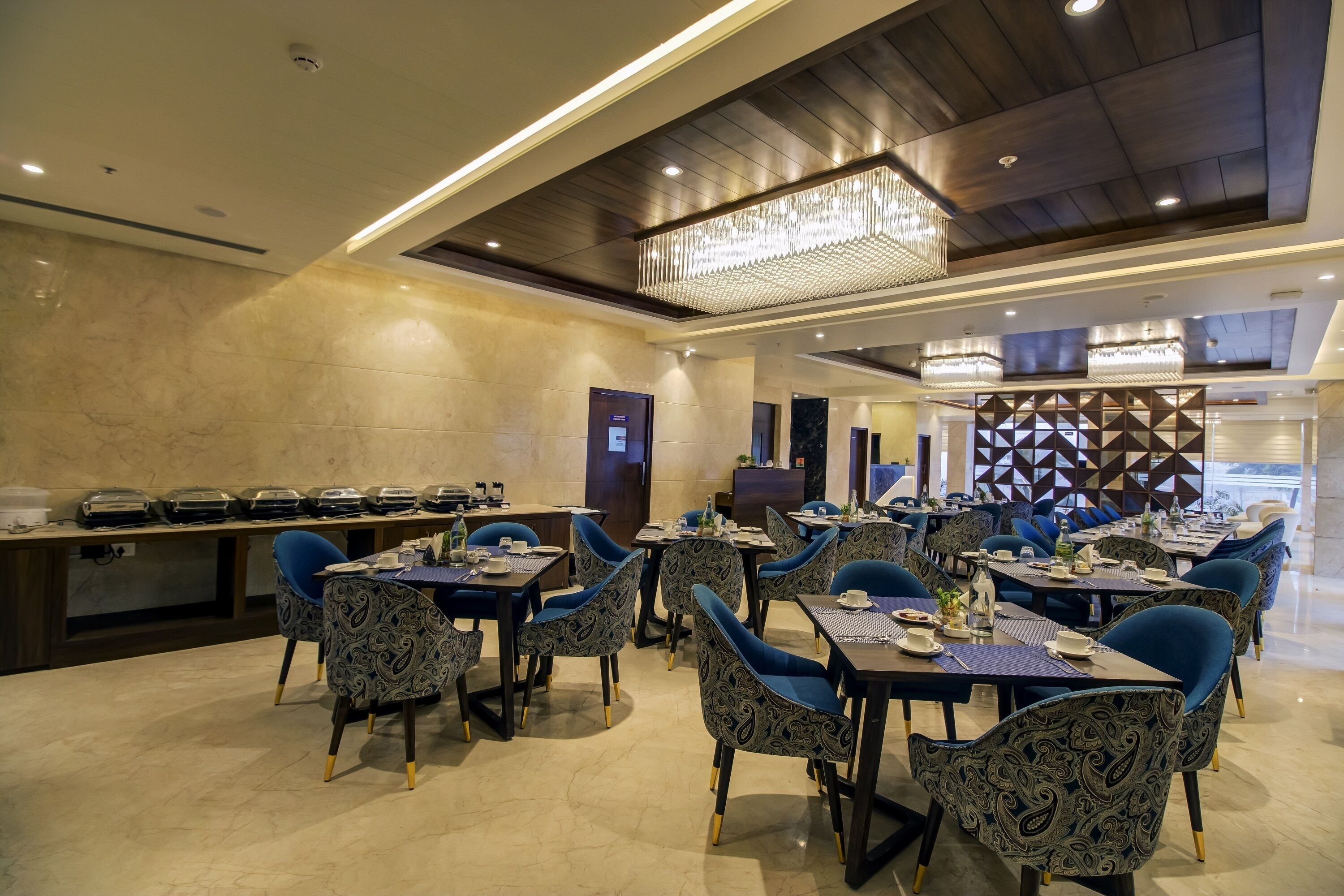 A modern dining area with patterned chairs, tables set with plates and cutlery, and a decorative wall with geometric patterns.