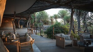 An outdoor dining area with wooden tables and chairs, surrounded by trees and a wooden deck. - Euphorbia Mashatu (Lentswelemoriti)