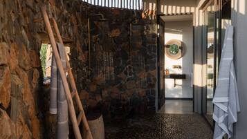 Experience a spa-like atmosphere in this unique bathroom with a stone wall, wooden ladder, and two showerheads.