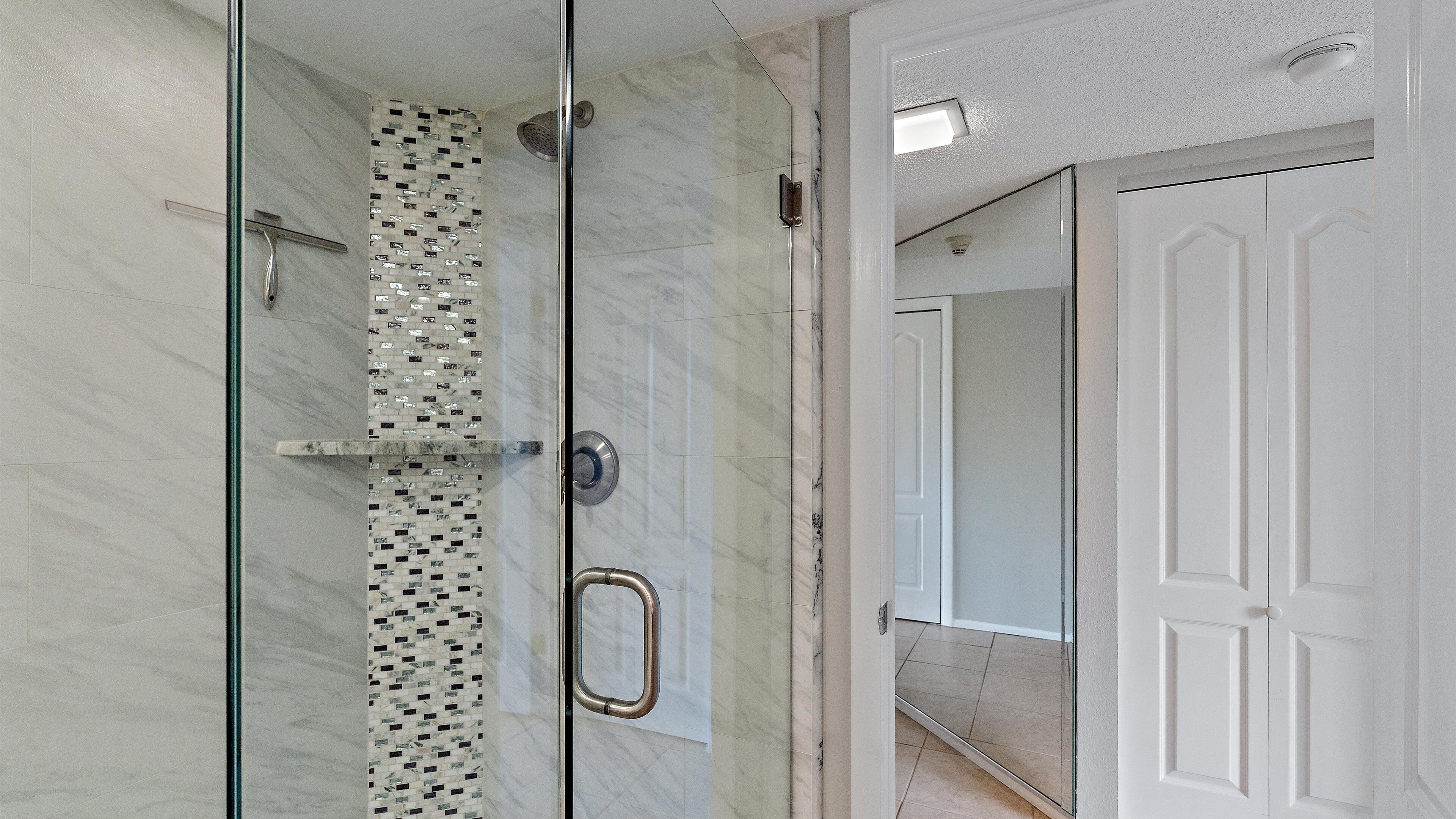 A modern bathroom with a glass shower enclosure, a tiled wall, and a white door.