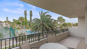 Un balcón con vista a una piscina, palmeras y una cancha de tenis.