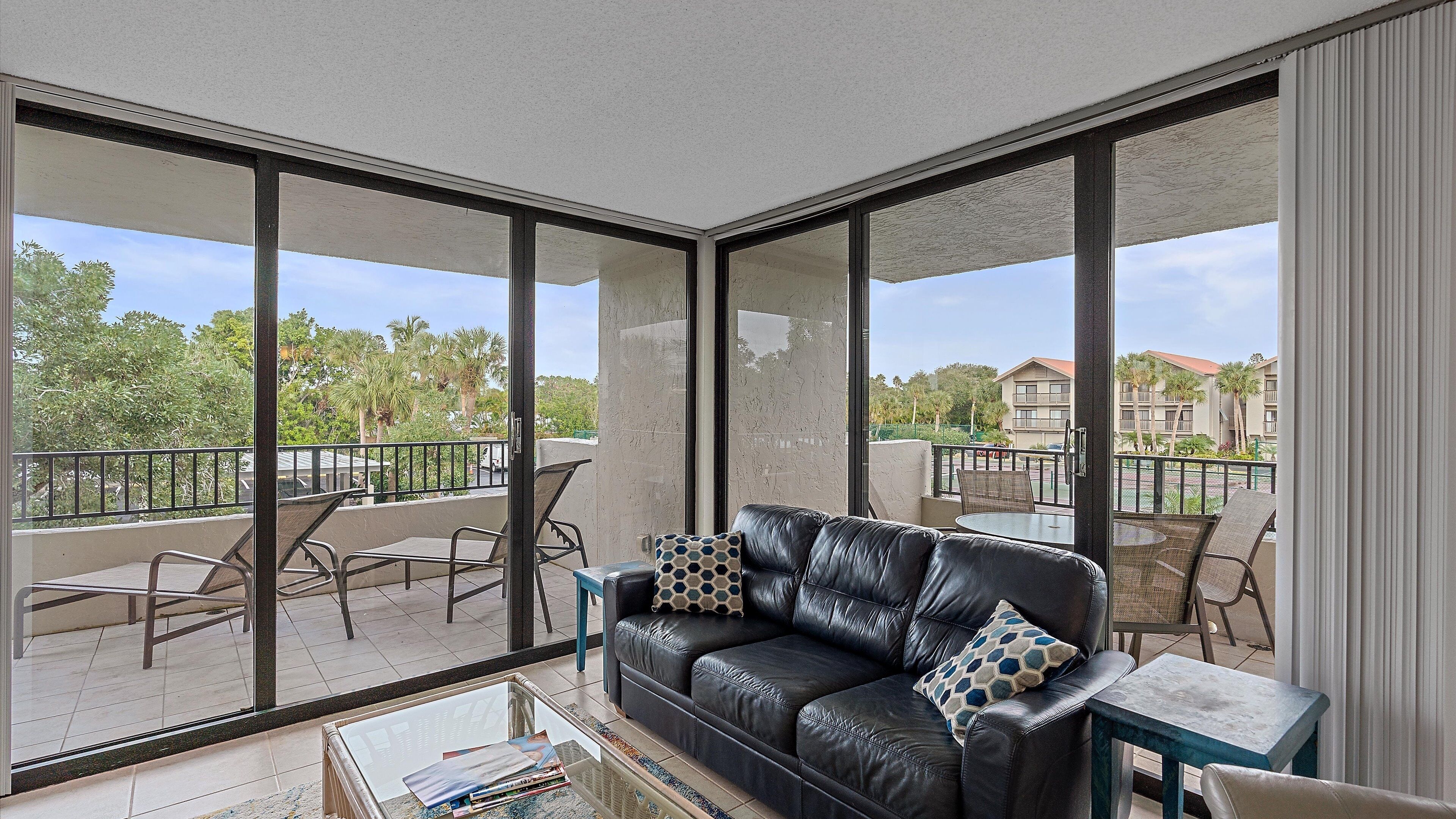 A balcony with a black leather sofa, two patterned cushions, a small table, and a chair.