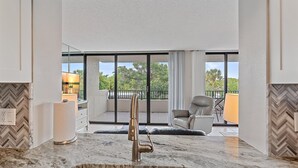 Una cocina moderna con encimera de mármol, grifo de acero inoxidable y vistas a un balcón con una silla y una mesa.