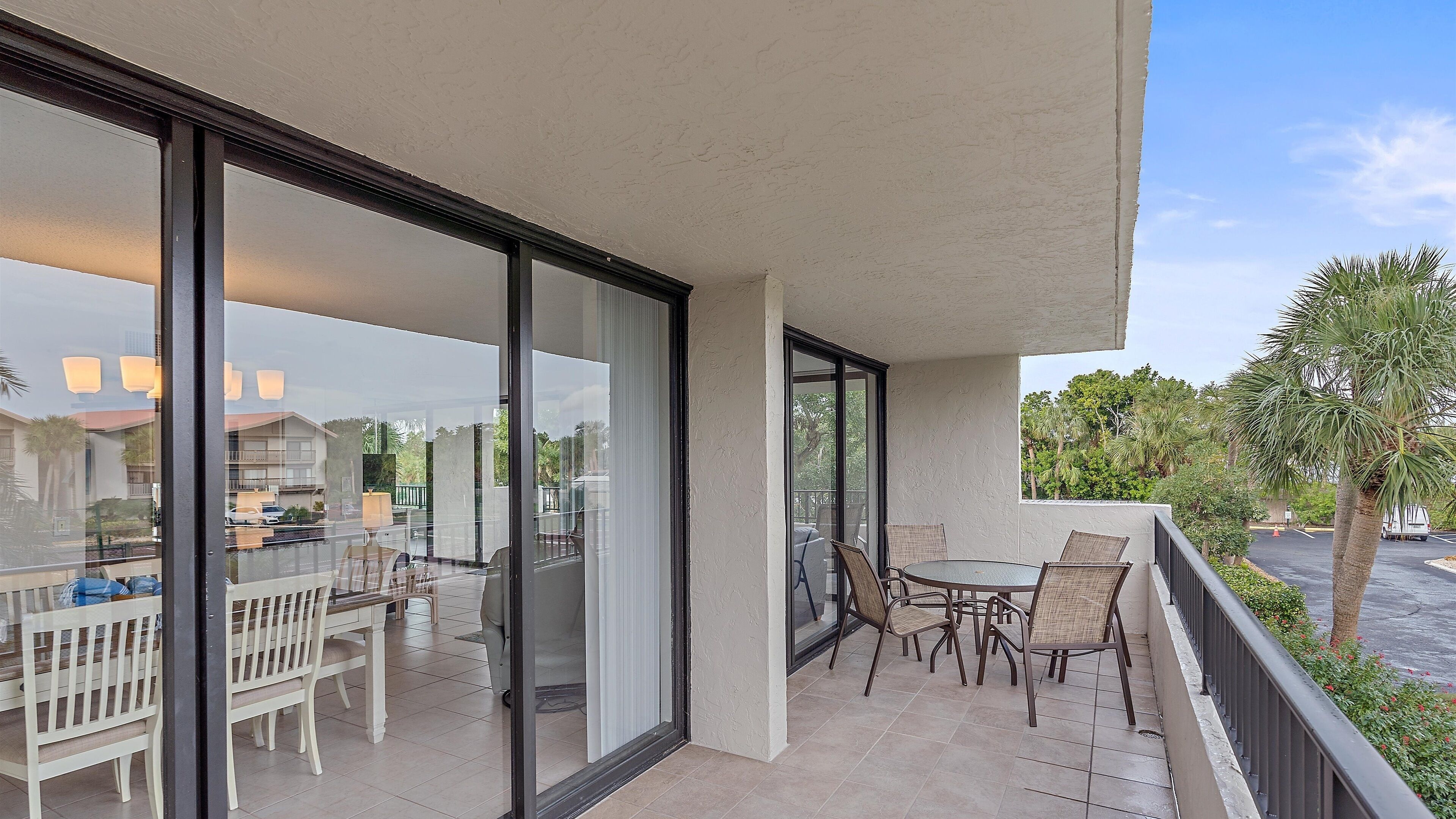 A balcony with a glass door, a dining table with chairs, and a view of the surrounding area.