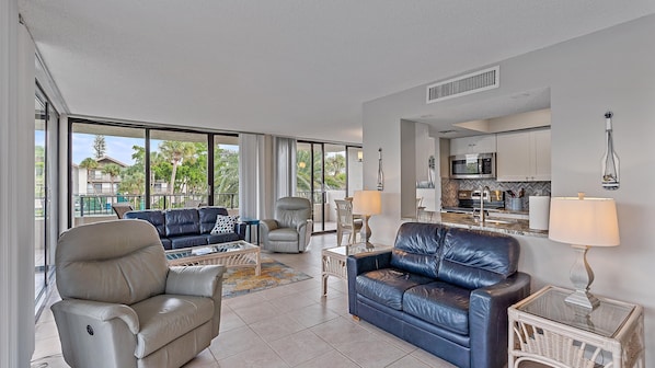 A spacious living area with a sofa, armchairs, a dining table, and a kitchen in the background.
