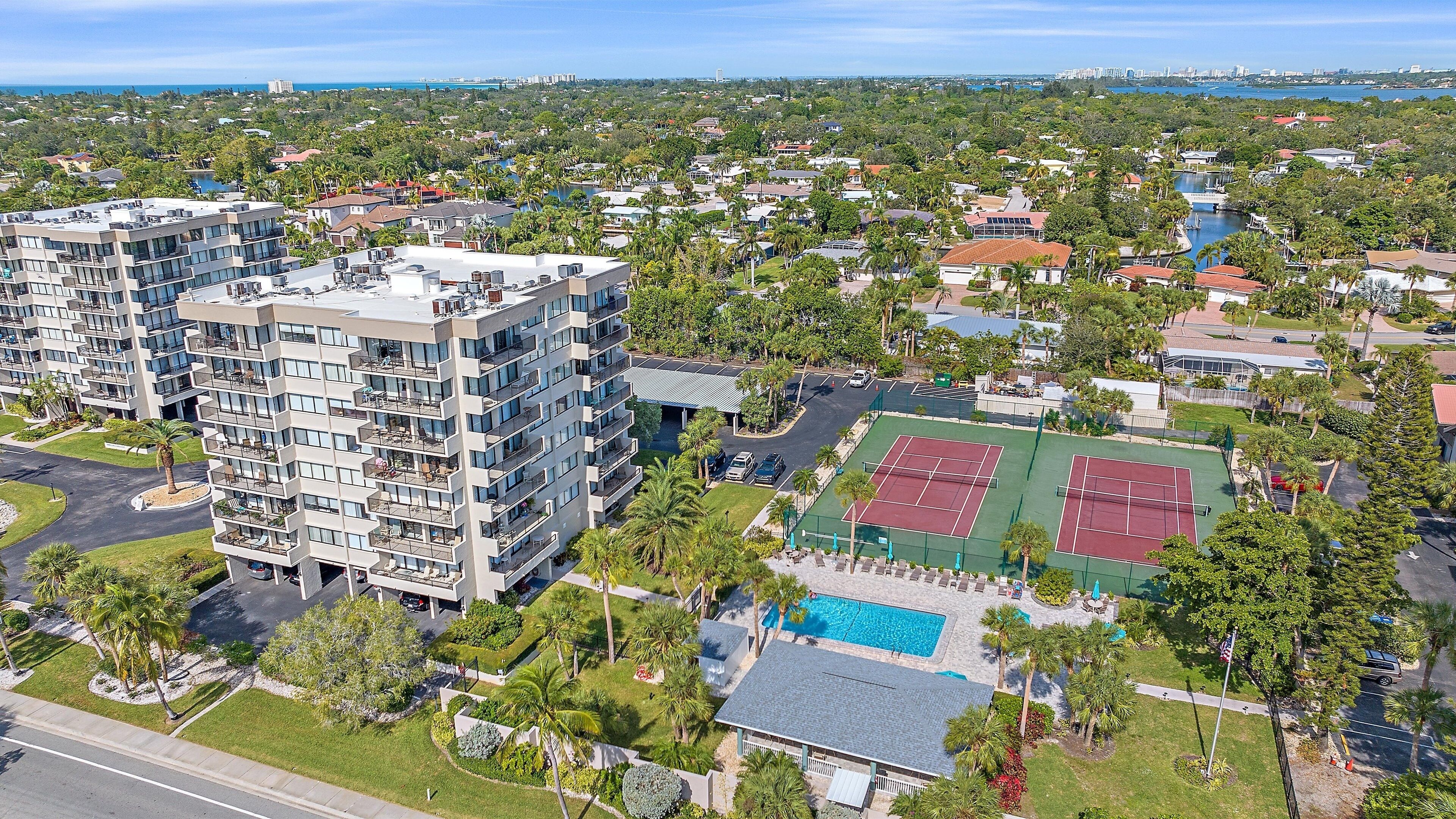 A high-rise building with multiple balconies, a tennis court, and a swimming pool.