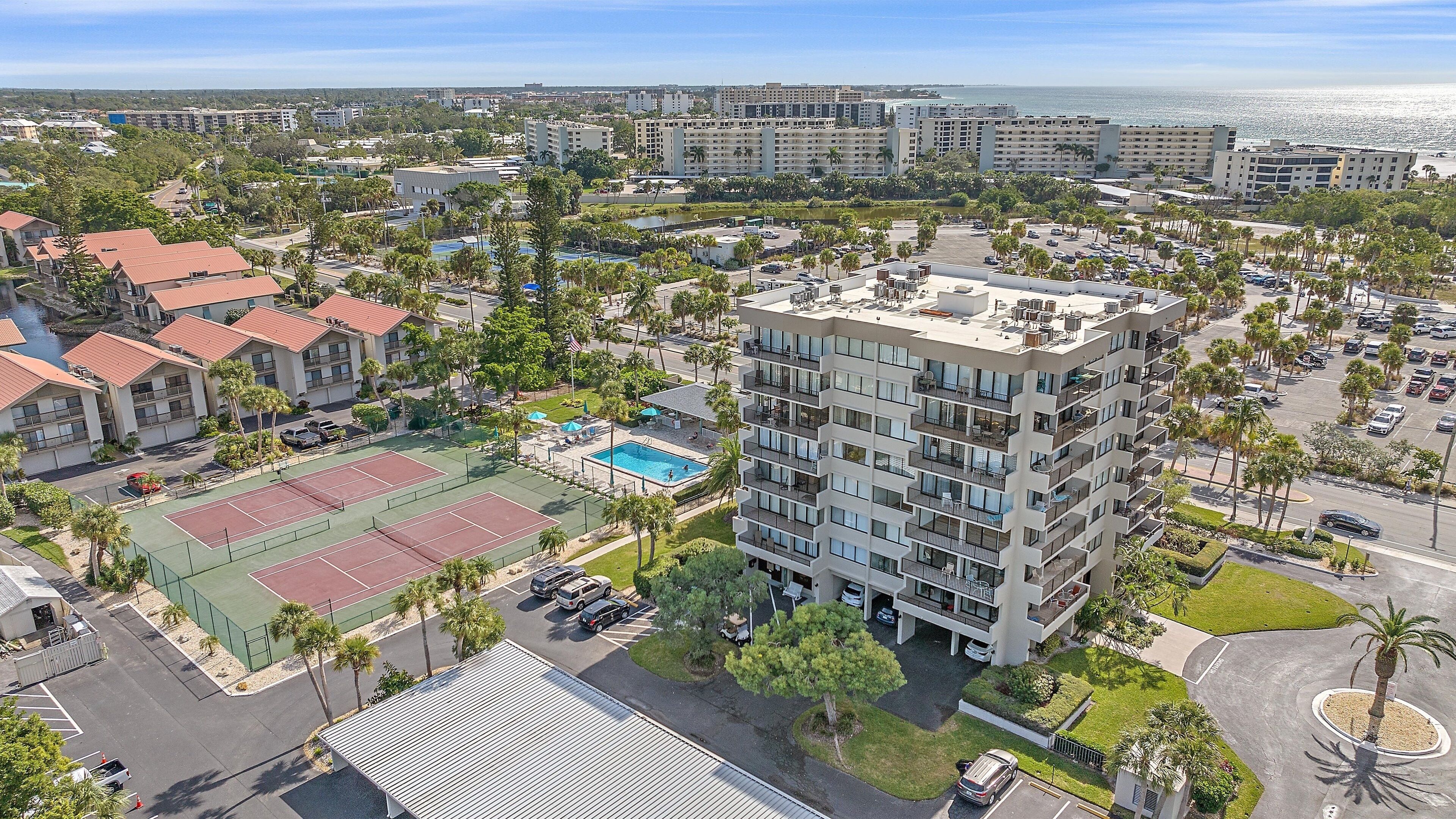 A multi-story hotel with a rooftop pool, tennis courts, and a view of the ocean.