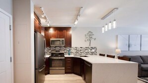 A modern kitchen with wooden cabinets, a stainless steel refrigerator, a microwave, and a large island with a sink. - Premium Unit 1307 - 1 Bedroom - Zephyr Mountain 1 Condo (Winter Park)
