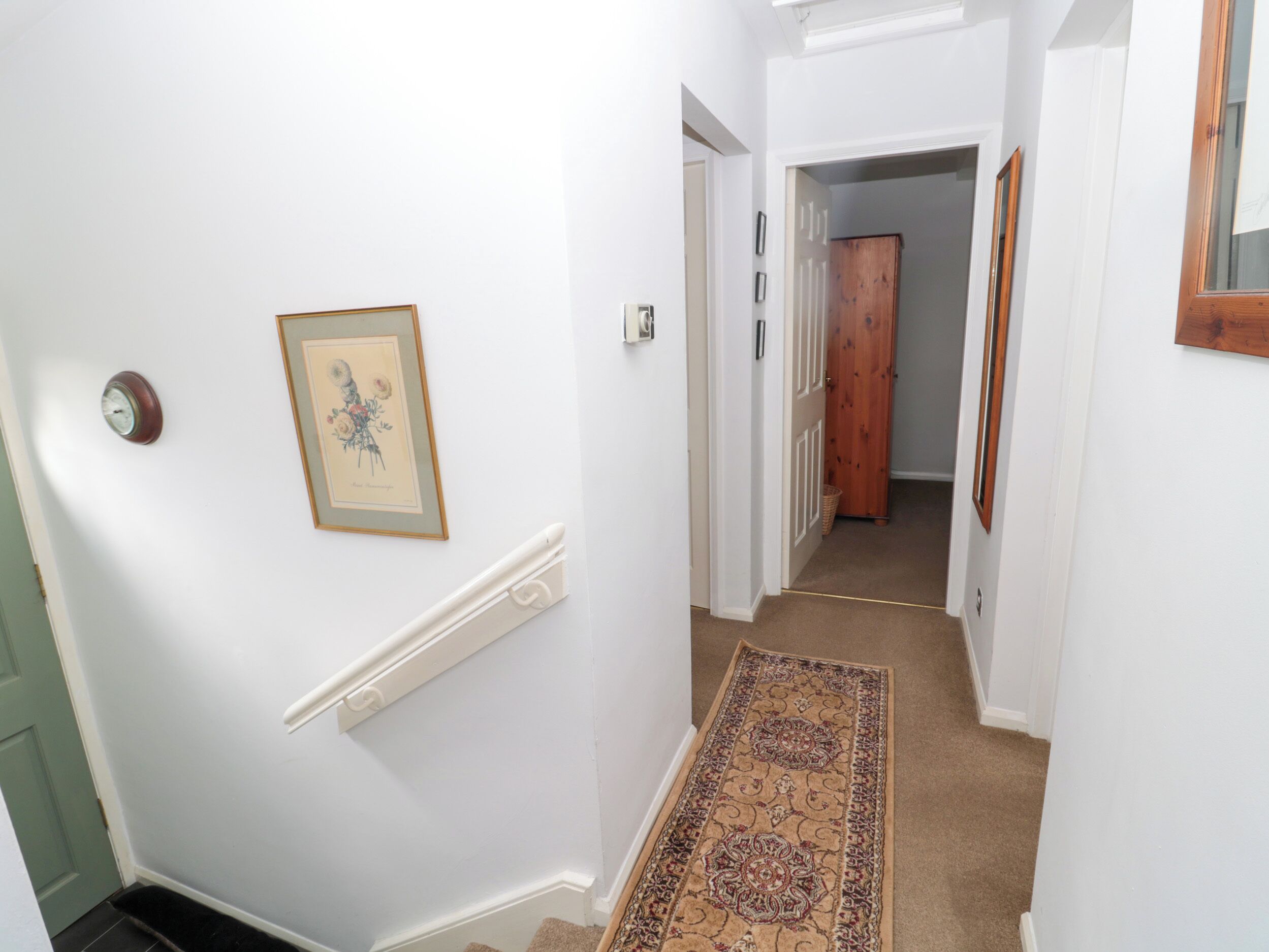 A hallway with white walls, a wooden door, and a patterned carpet.