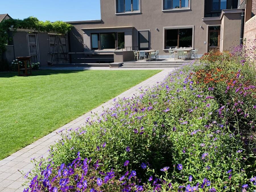 Een modern gebouw met twee verdiepingen, een plat dak, grote ramen en een bestraat terras met buitenmeubels.