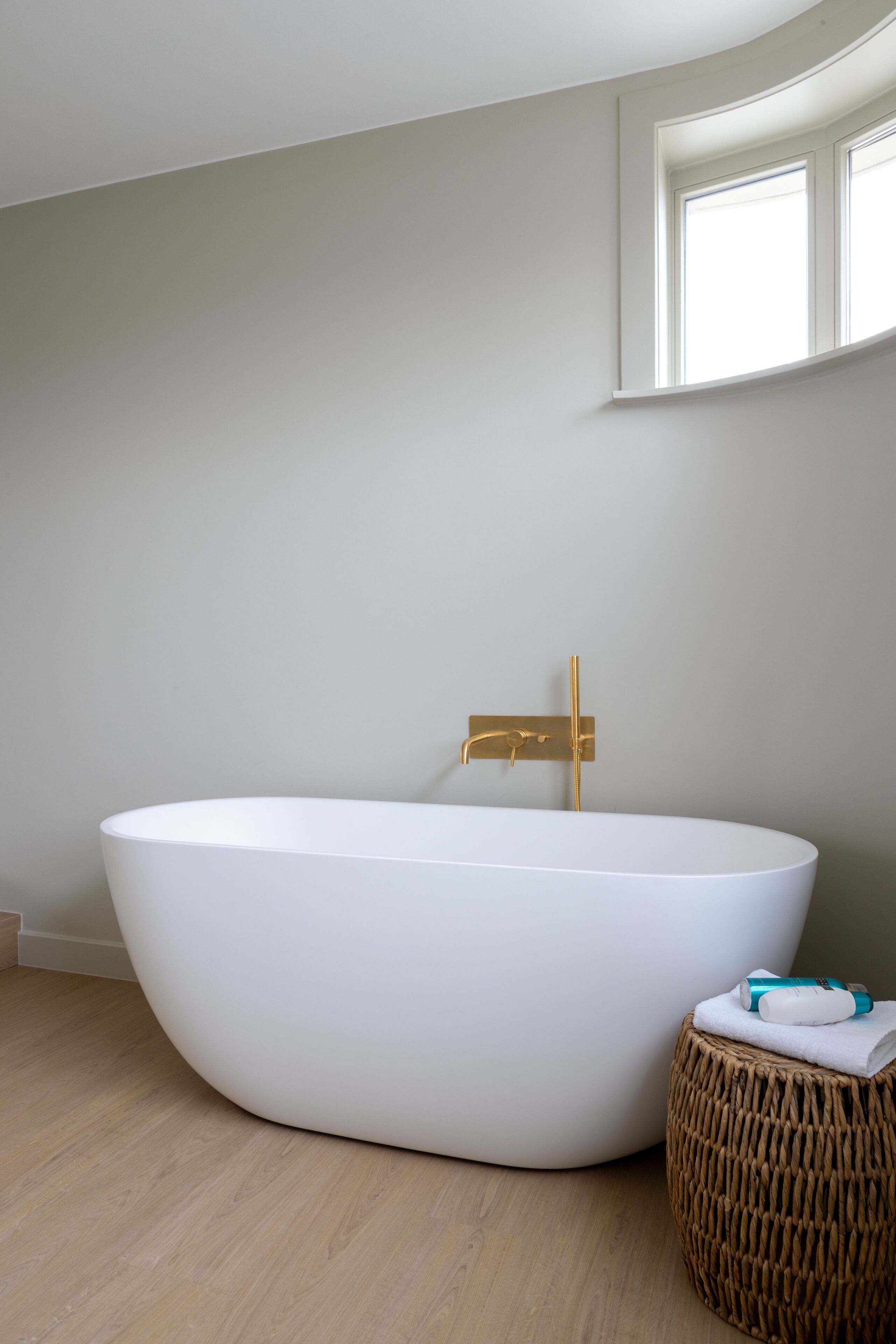 A modern bathroom with a freestanding bathtub, a wooden floor, and a window above the tub.