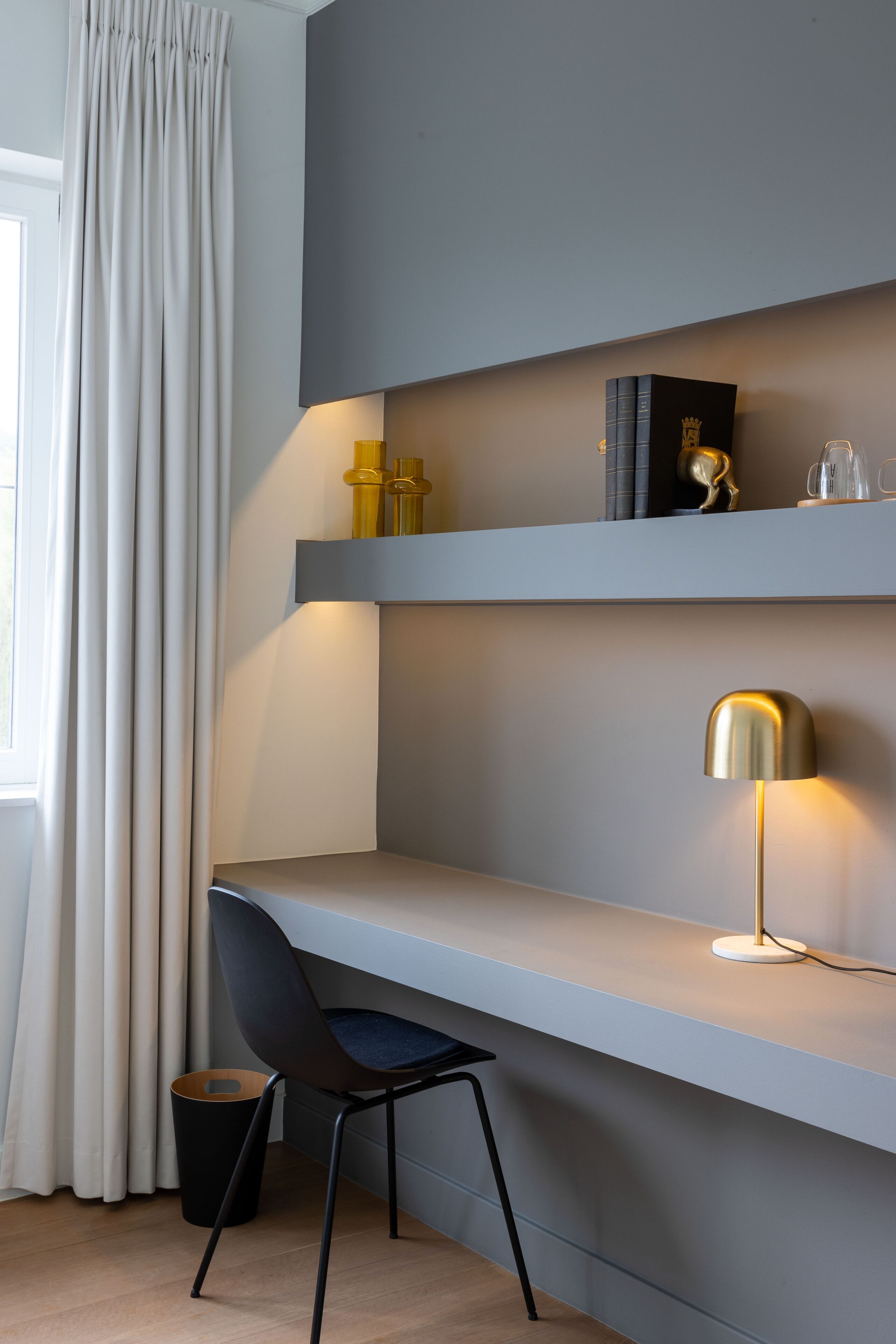 A modern desk with a chair, a lamp, and a shelf with books and decorative items.