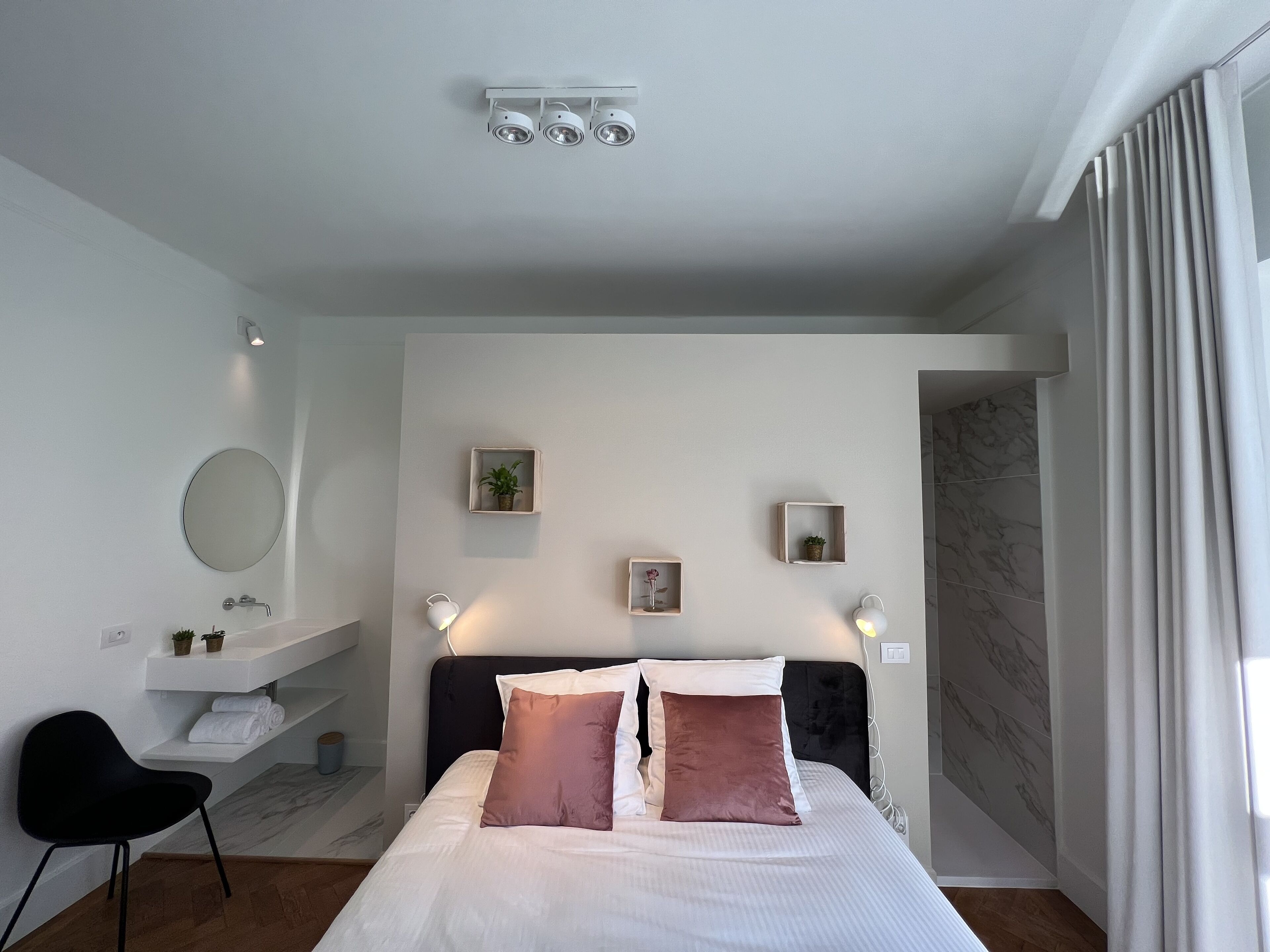 Une chambre moderne comprenant un lit, des tables de chevet, un miroir et une salle de bain avec un lavabo et un porte-serviettes.