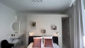 Une chambre moderne comprenant un lit, des tables de chevet, un miroir et une salle de bain avec un lavabo et un porte-serviettes.