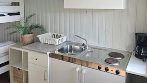 Una kitchenette compacta con estufa, lavamanos y armarios blancos.