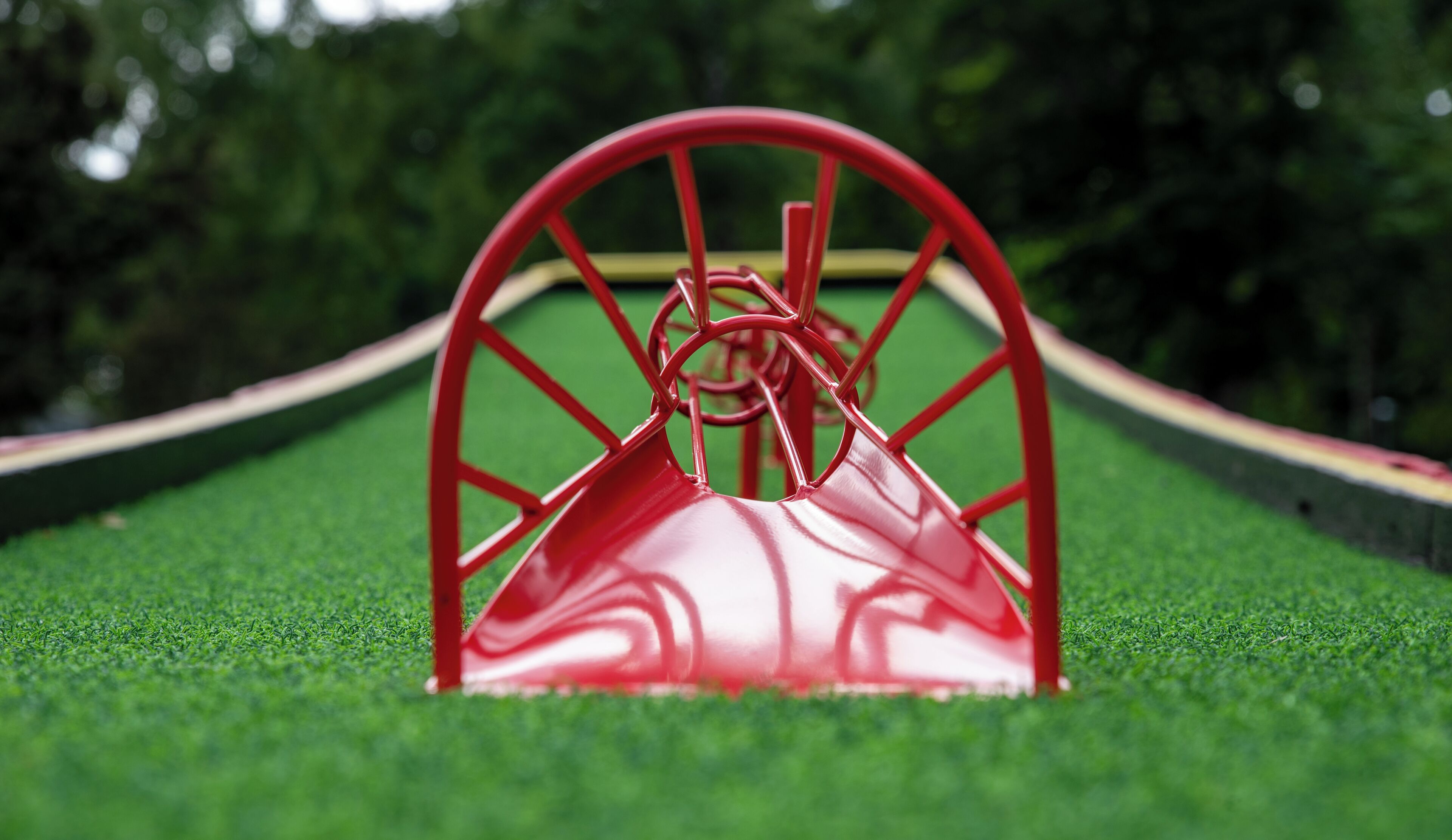Un tobogán metálico rojo sobre césped artificial, con un fondo verde.