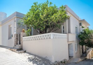 A modern two-story building with a tree in front, a white fence, and a clear blue sky. - Sofia's Lemontree! Amazing apartment in the center of the city! (Agios Nikolaos)