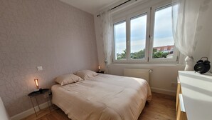 Un dormitorio con cama, mesitas de noche, un radiador y una ventana con cortinas.