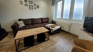 Una sala de estar con un sofá de cuero marrón, una mesa de centro de madera, un sillón de mimbre y un televisor sobre un mueble.