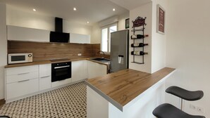 Una cocina moderna con microondas, horno y refrigerador. Se observa una cava de vinos en la pared y una barra con dos taburetes.