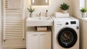 A modern bathroom with a built-in washing machine, a sink with a mirror, and a towel rack.
